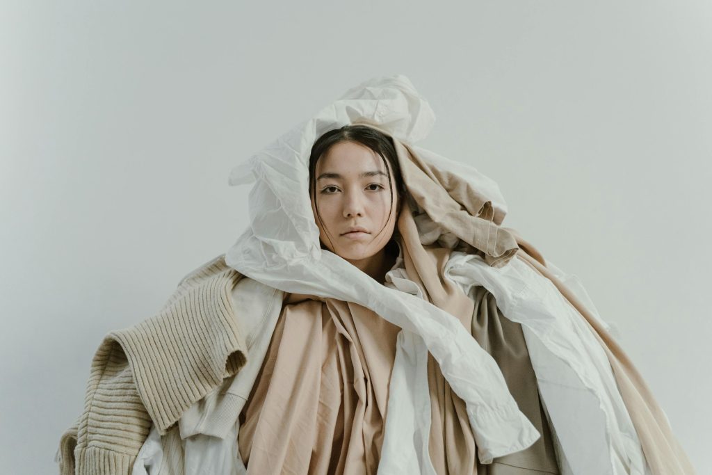 Artistic portrait of a woman in a pile of neutral toned clothes.