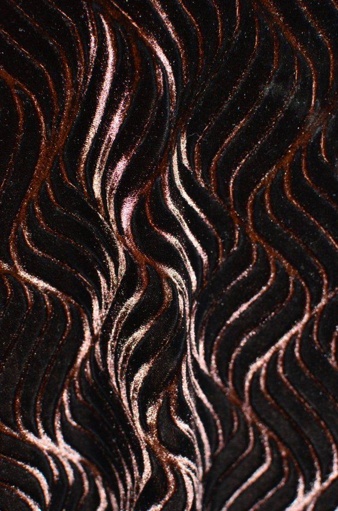 Textured seamless abstract background with wiggle pattern creating wavy ornament on dark thick fabric with creative design and glossy surface