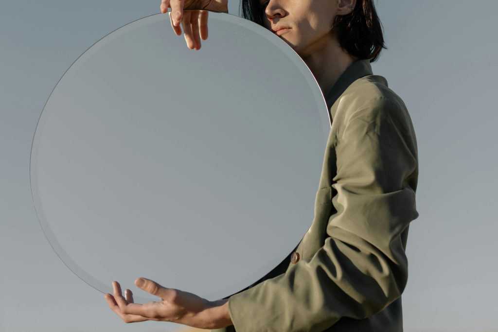 pexels-photo-5103885-5103885 A stylish individual holding a round mirror outdoors, reflecting the sky.
